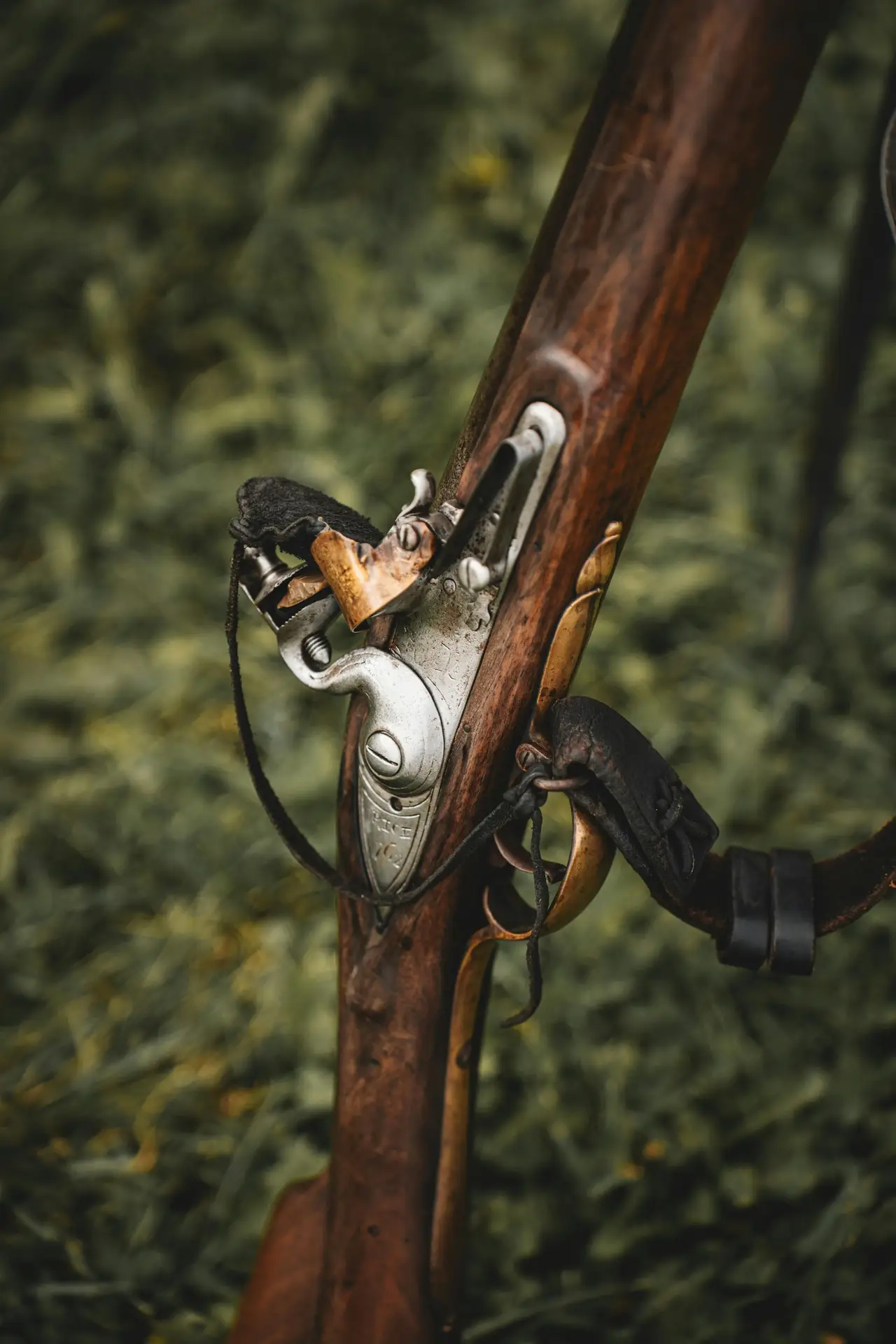 Detailed close-up of an antique rifle's mechanism set against a grassy background, showcasing vintage craftsmanship.